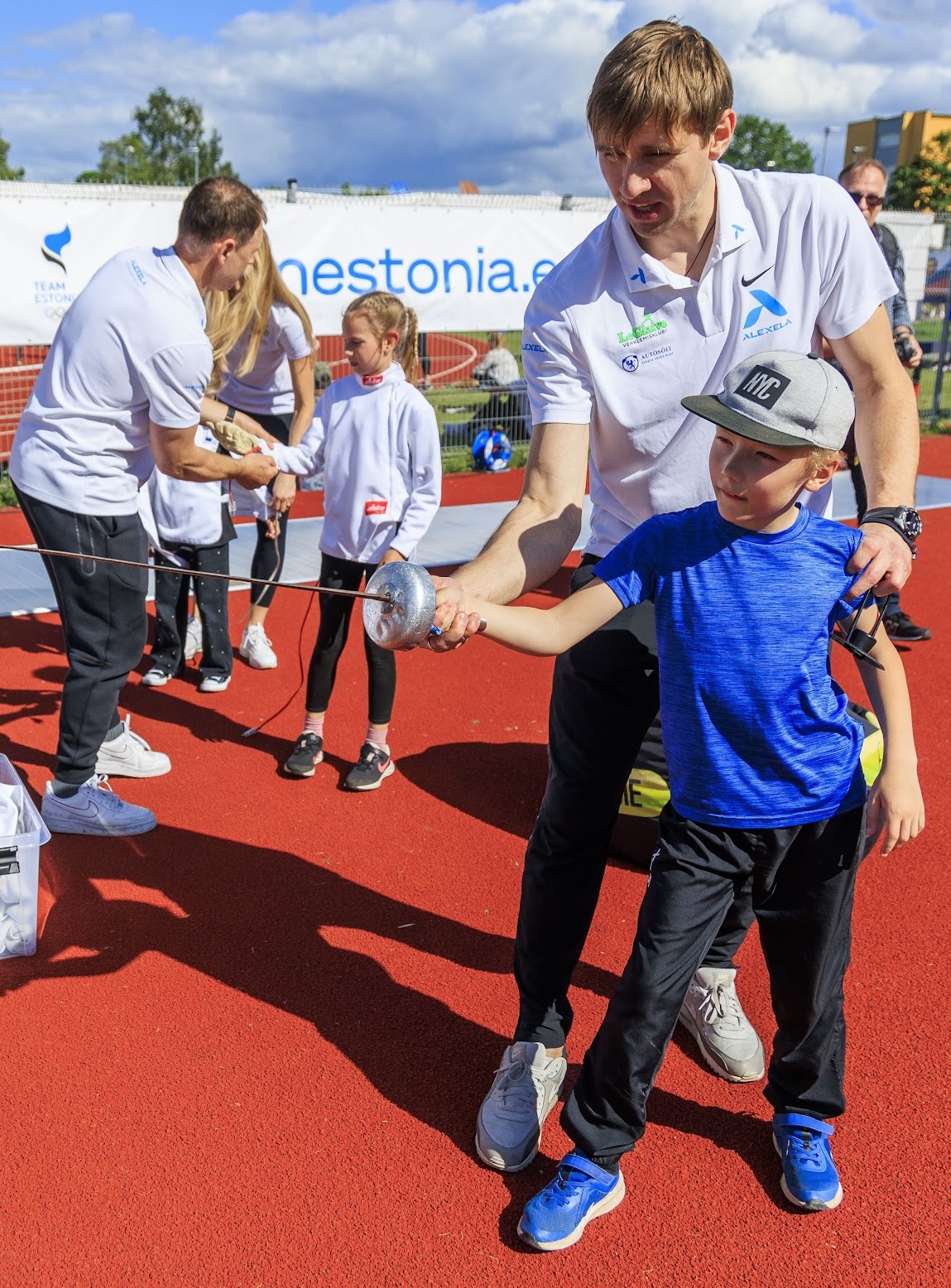 Two coaches guide children as they try fencing