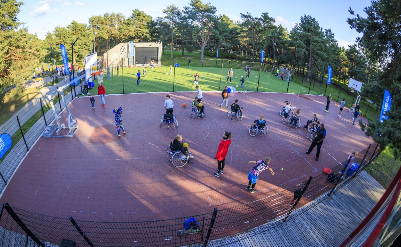 Children and instructors explore ball games on an outdoor court, including wheelchair basketball